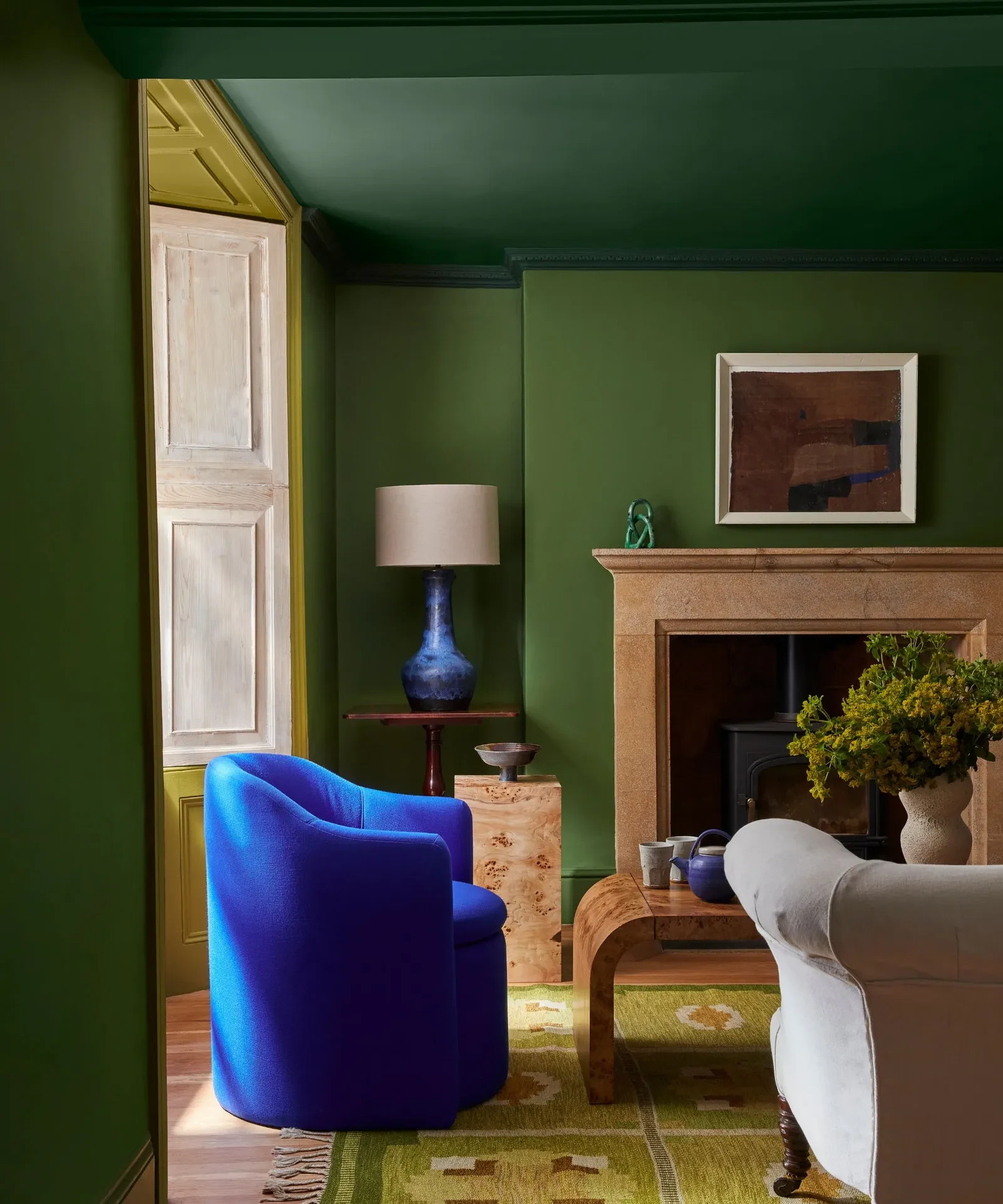 A green painted living room with a blue armchair and stone fireplace