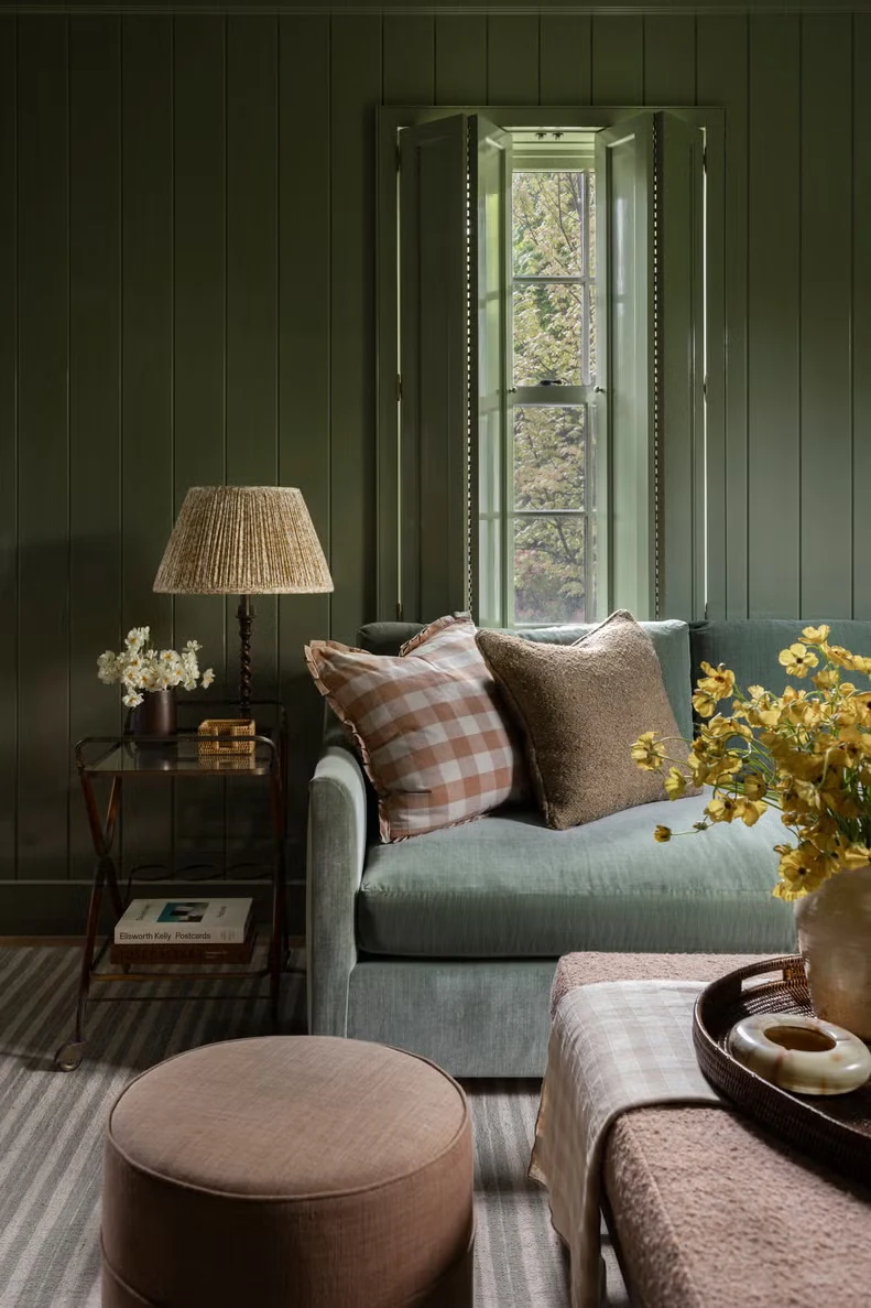 A sage green paneled living room with a velvet sofa